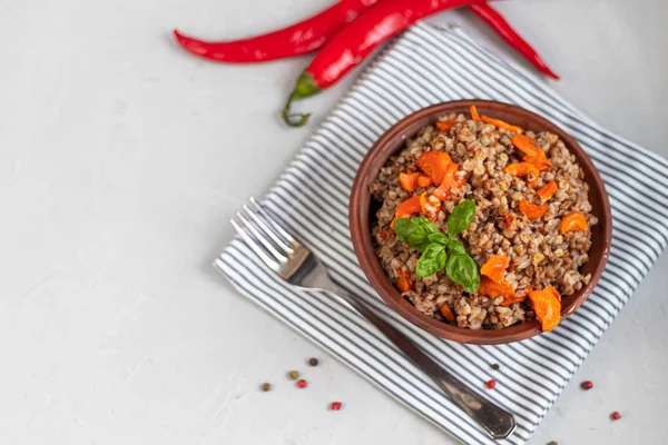 Haşlanmış havuçlu karabuğday lapası. Yeşil yapraklarla süslenmiş. Pamuk peçeteye, açık gri üzerine .