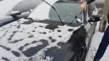 Cleaning the car that was snowing. Winter cold morning, black car in the parking lot.