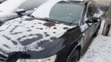 Cleaning the car that was snowing. Winter cold morning, black car in the parking lot.