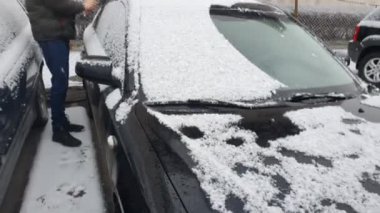 Cleaning the car that was snowing. Winter cold morning, black car in the parking lot.