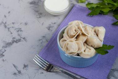Yeşil soğanlı haşlanmış hamur tatlısı. Arka planda ekşi kremalı bir kase var. Betonun altındaki gri arka planda.