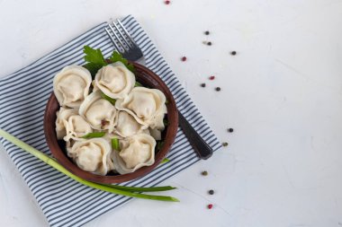 Yeşil soğanlı haşlanmış hamur tatlısı. Arka planda yeşiller, kırmızı biber ve defne yaprakları var. Şeffaf bir kaymak kabında.