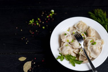 Yeşil soğanlı haşlanmış hamur tatlısı. Arka planda yeşiller, kırmızı biber ve defne yaprakları var. Siyah ahşap arka planda.