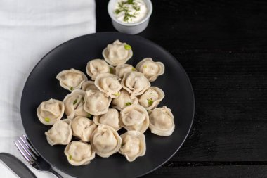 Haşlanmış börek. Arka planda yeşiller, kırmızı biber ve defne yaprakları var. Beyaz peçeteyle siyah ahşap bir arka planda.