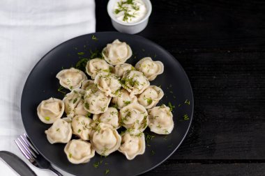 Haşlanmış börek. Arka planda yeşiller, kırmızı biber ve defne yaprakları var. Beyaz peçeteyle siyah ahşap bir arka planda.