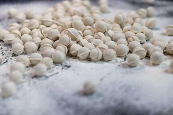 Meel giet op de tafel. Om deegproducten te maken, zitten minidumplings niet vast. Dumplings vallen in bloem. Donker gemarmerde achtergrond. — Stockfoto