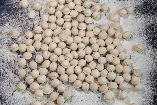 Meel giet op de tafel. Om deegproducten te maken, zitten minidumplings niet vast. Dumplings vallen in bloem. Donker gemarmerde achtergrond. — Stockfoto