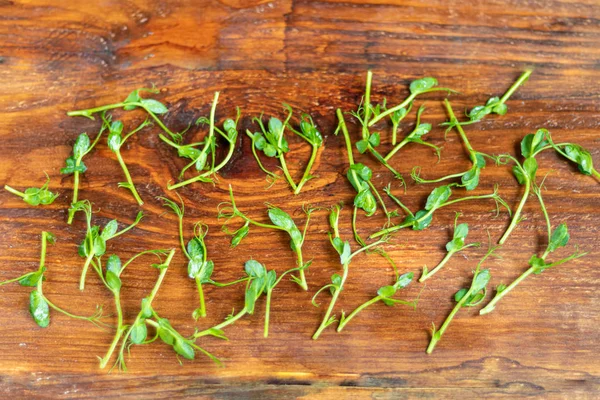 On a wooden surface lies a green microgreen from pea seedlings. Healthy eating . — Stock Photo, Image