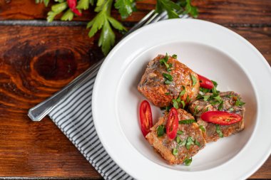 Morina filetosu ya da beyaz tabakta diğer balıklar. Domates ve soğanla pişirilmiş. Bezelyeler yeşil yapraklar ve fidanlardan çıkan mikroyeşillerle serpiştirilir. Ahşap bir arka planda.