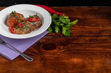 Morina filetosu ya da beyaz tabakta diğer balıklar. Domates ve soğanla pişirilmiş. Bezelyeler yeşil yapraklar ve fidanlardan çıkan mikroyeşillerle serpiştirilir. Ahşap bir arka planda.