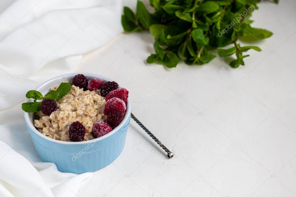 Breakfast consisting of oatmeal, nuts and fruits. Kiwi raspberries blackberries pomegranates almonds mint decorate a plate. Healthy eating, on a light background.