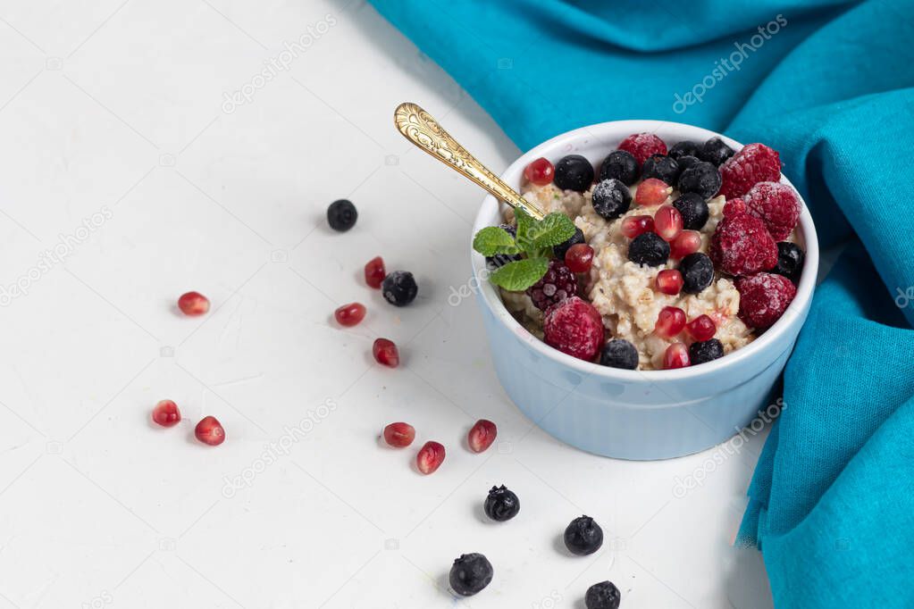 Breakfast consisting of oatmeal, nuts and fruits. Kiwi raspberries blackberries pomegranates almonds mint decorate a plate. Healthy eating, on a light background.