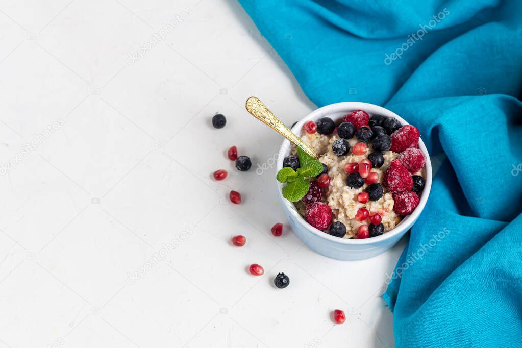 Breakfast consisting of oatmeal, nuts and fruits. Kiwi raspberries blackberries pomegranates almonds mint decorate a plate. Healthy eating, on a light background.