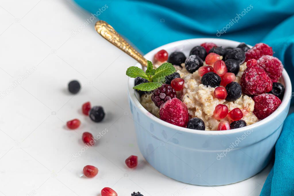 Breakfast consisting of oatmeal, nuts and fruits. Kiwi raspberries blackberries pomegranates almonds mint decorate a plate. Healthy eating, on a light background.