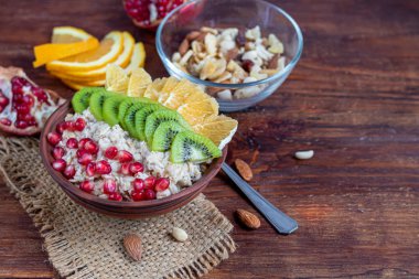 Yulaf ezmesi, fındık ve meyvelerden oluşan kahvaltı. Kivi muzlu nar bademleri bir tabak süsler. Sağlıklı yemek, ahşap arka planda..