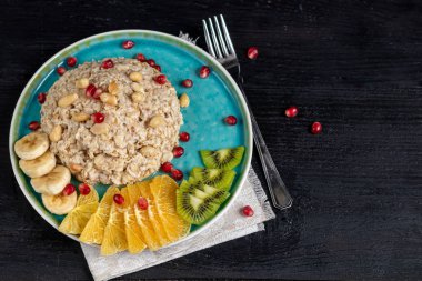 Breakfast consisting of oatmeal, nuts and fruits. Kiwi, banana, pomegranate and almonds decorate the plate. Healthy food, on a dark wooden background.