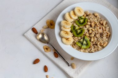 Breakfast consisting of oatmeal, nuts and fruits. Kiwi, banana, pomegranate and almonds decorate the plate. Healthy food, on a white background.