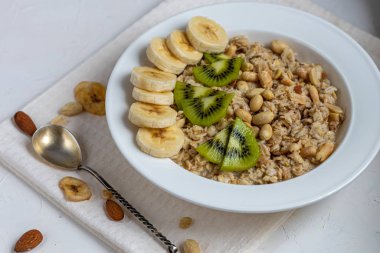 Breakfast consisting of oatmeal, nuts and fruits. Kiwi, banana, pomegranate and almonds decorate the plate. Healthy food, on a white background.