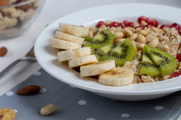 Śniadanie składające się z owsianki, orzechów i owoców. Kiwi, banan, granat i migdały zdobią talerz. Zdrowa żywność, na białym tle. — Zdjęcie stockowe