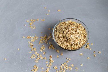Raw oatmeal in a transparent bowl, prepared for brewing porridge. Healthy food, on a gray background.