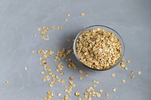 Farina d'avena cruda in una ciotola trasparente, preparata per la preparazione del porridge. Cibo sano, su sfondo grigio . — Foto Stock