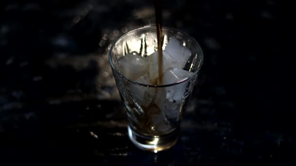暗い背景に透明なガラスに氷を注ぐ その後 同じ場所に黒ソーダ水とレモネードを注ぎます — ストック動画