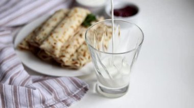 Breakfast with pancakes and milk. Milk is poured into a transparent glass. In the background is a plate and a fresh napkin. Copy space.