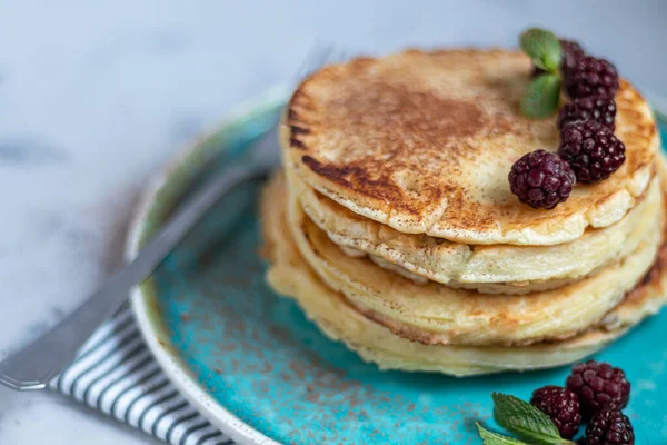 Una pila de deliciosos panqueques con frambuesas, moras y arándanos. Sobre un fondo claro. Espolvoreado con azúcar glaseado y decorado — Foto de Stock