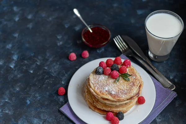 Una pila de deliciosos panqueques con frambuesas, moras y arándanos. Sobre un fondo de piedra oscura. Espolvoreado con azúcar glaseado y decorado — Foto de Stock