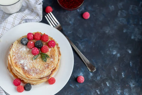 Una pila de deliciosos panqueques con frambuesas, moras y arándanos. Sobre un fondo de piedra oscura. Espolvoreado con azúcar glaseado y decorado — Foto de Stock