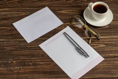 Üzerinde bir sürü şey olan ahşap bir ofis masası. Kalemle günlük, Samsung telefonu. Bir fincan beyaz kahve. Kopyalama alanı olan üst görünüm,