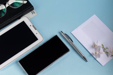 A light blue table with the necessary items on it. Diary with pen, Samsung phone. White cup of coffee. Top view with copy space,