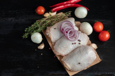 On brown paper, fresh skinless chicken thighs, next to mushrooms, with tomatoes, red onions and thyme. Recipe of dish. Ingredients.