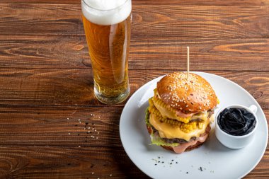 Biftek, domates, peynir, salatalık ve salatalı leziz ızgara burger. Yakınlarda temiz eller ve bir bardak bira için siyah lastik eldivenler var..