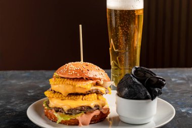 Biftek, domates, peynir, salatalık ve salatalı leziz ızgara burger. Yakınlarda temiz eller ve bir bardak bira için siyah lastik eldivenler var..