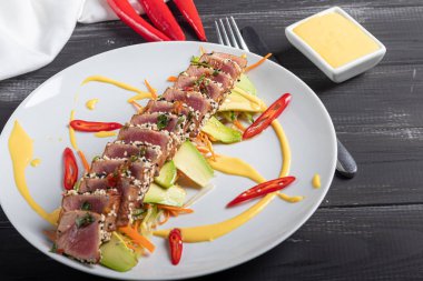 Japon yemeği. Ton balıklı Tataki. Susamlı kızarmış balık, soya sosu, wasabi, limon. Sebze yastığının üzerinde. Avokadolar, acı biber şeritleri.