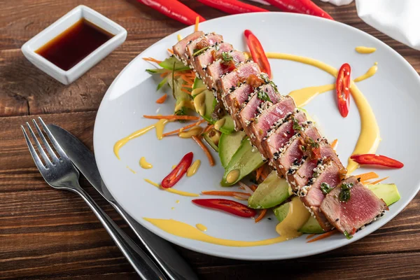 Japon yemeği. Ton balıklı Tataki. Susamlı kızarmış balık, soya sosu, wasabi, limon. Sebze yastığının üzerinde. Avokadolar, acı biber şeritleri.