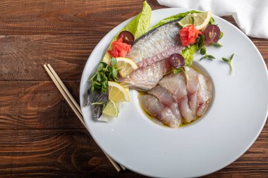 Hafif tuzlu dorado ve trüf yağlı ayçiçeği. Limon, limon, üzüm ve zencefil turşusunun yanında. Tabağın kenarında yemek çubukları var..