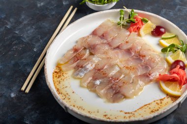 Hafif tuzlu dorado ve trüf yağlı ayçiçeği. Limon, limon, üzüm ve zencefil turşusunun yanında. Tabağın kenarında yemek çubukları var..