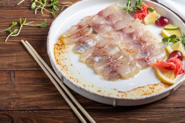 Hafif tuzlu dorado ve trüf yağlı ayçiçeği. Limon, limon, üzüm ve zencefil turşusunun yanında. Tabağın kenarında yemek çubukları var..