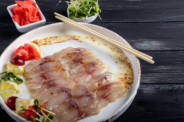 Hafif tuzlu dorado ve trüf yağlı ayçiçeği. Limon, limon, üzüm ve zencefil turşusunun yanında. Tabağın kenarında yemek çubukları var..