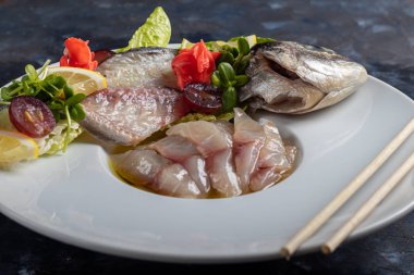 Hafif tuzlu dorado ve trüf yağlı ayçiçeği. Limon, limon, üzüm ve zencefil turşusunun yanında. Tabağın kenarında yemek çubukları var..