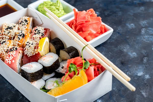 A box of sushi Nigiri, Uramaki California, Philadelphia, on a black stone plate. Sushi menu in a white transport box on a wooden background.