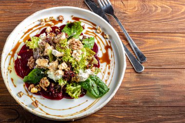 Cevizli pancar carpaccio, keçi peyniri, marul ve ıspanak. Sosla kaplanmış. Derin bir tabakta, karanlık bir arka planda..