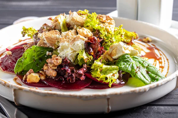 Carpaccio de betterave aux noix, fromage de chèvre, laitue et épinards. Vêtue de sauce. Sur un fond sombre . — Photo