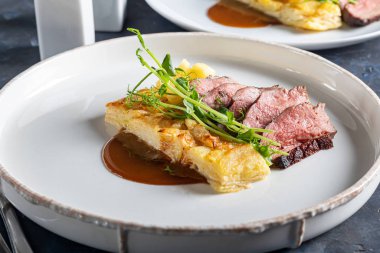 Yanında patates güveci olan ördek göğsü. Bezelye mikroyeşili, domates ve biber soslu. Beyaz bir tabakta. Ahşap bir arka planda,