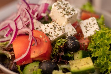 Greek vegetable salad. It consists of tomatoes, olives, feta cheese, herbs, cucumbers and red onions. On a wooden background.