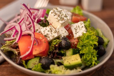 Greek vegetable salad. It consists of tomatoes, olives, feta cheese, herbs, cucumbers and red onions. On a wooden background.