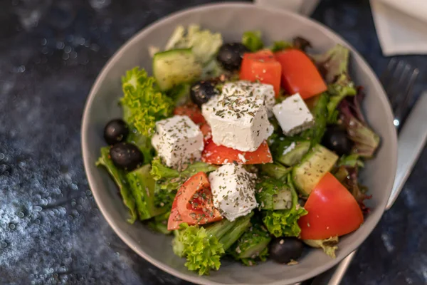 Greek vegetable salad. It consists of tomatoes, olives, feta cheese, herbs, cucumbers and red onions. On a wooden background. — 图库照片