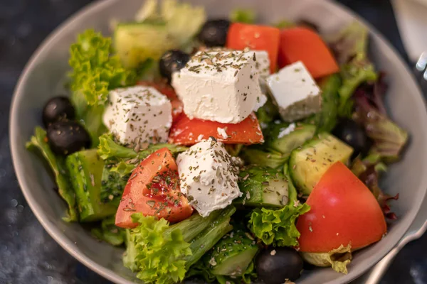 Greek vegetable salad. It consists of tomatoes, olives, feta cheese, herbs, cucumbers and red onions. On a wooden background. — 图库照片